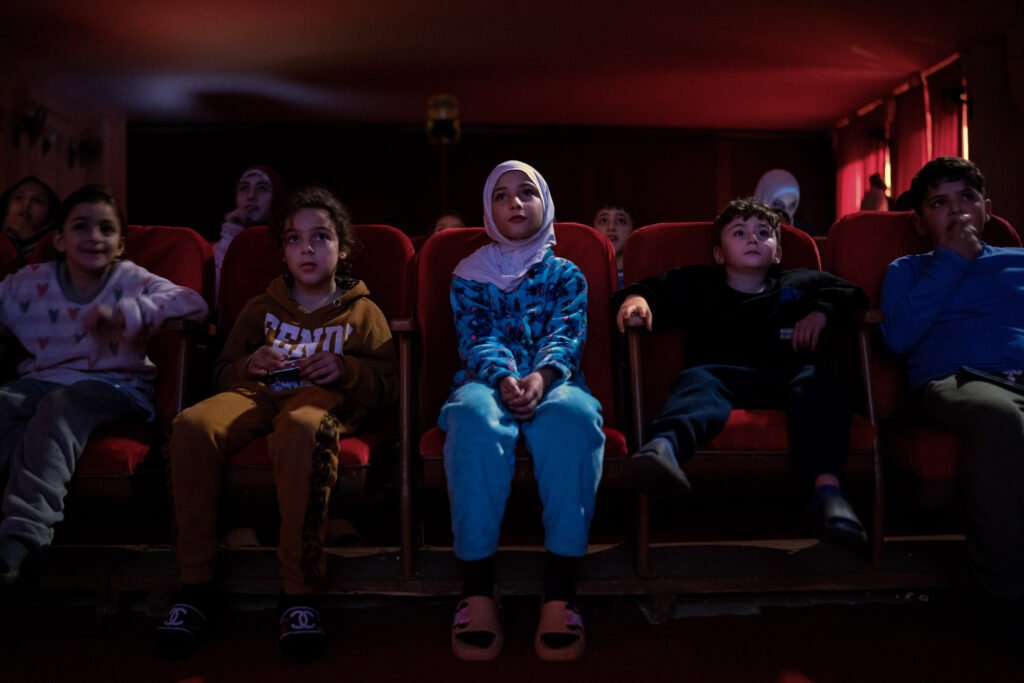 LIBAN, Beyrouth, 15 mars 2026.
Dans le cinéma Colisée, à Beyrouth. Le cinéma, géré par l’association Tiro, est reconverti en centre d’accueil pour les réfugiés du Sud-Liban depuis la reprise du conflit entre le Hezbollah et Israel, début mars 2026.
Des enfants réfugiés du Sud Liban viennent à une séance de cinéma organisée pour les jeunes au cinéma Colisée.